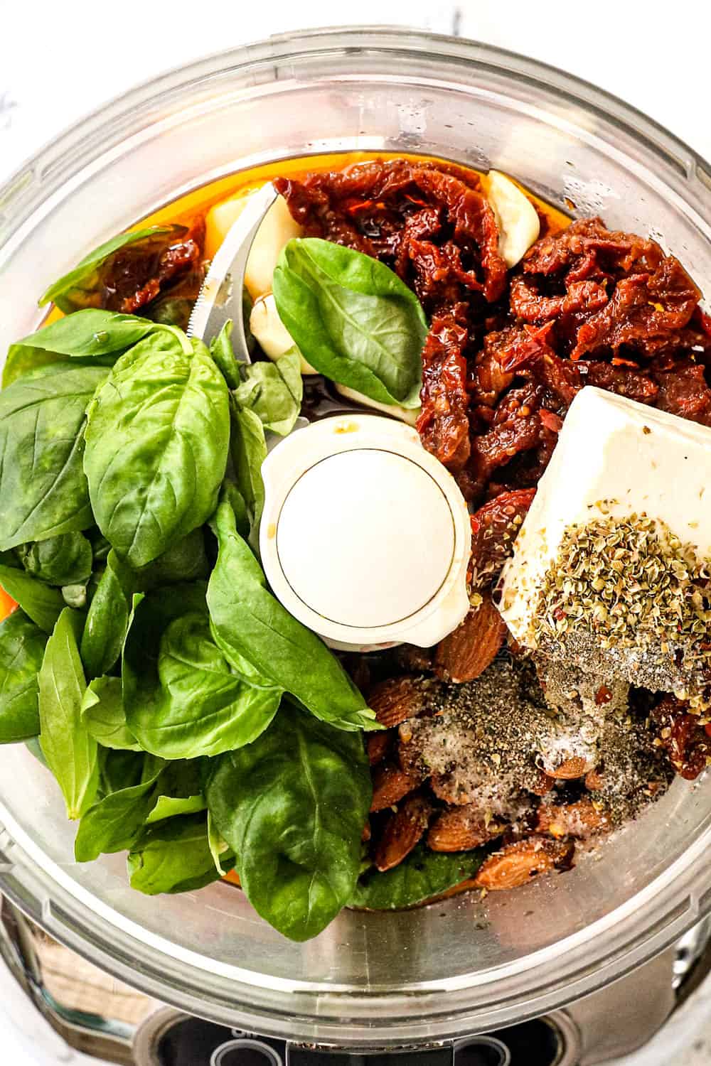 showing how to make the dressing for Greek couscous salad recipe by adding basil, sun dried tomato, feta and almonds to a food processor