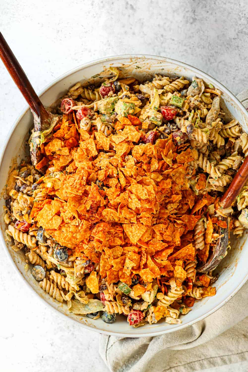 showing how to make taco pasta salad recipe by adding crushed nacho Doritos to the pasta salad