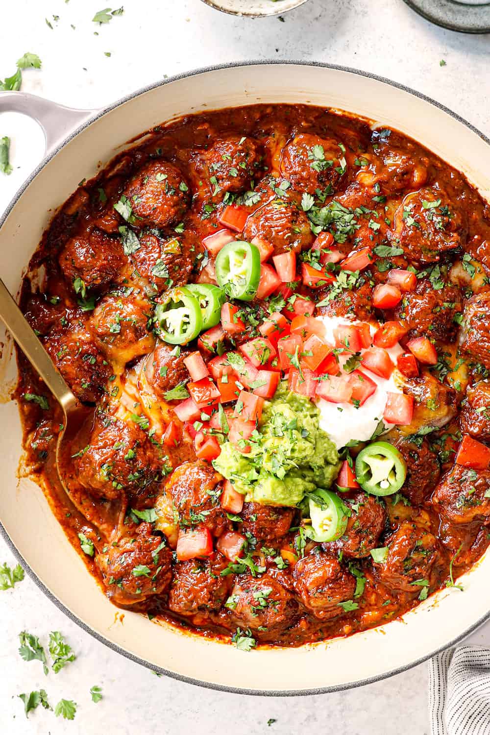 top view of baked enchilada meatballs in skillet topped with sour cream, guacamole, cilantro and tomatoes