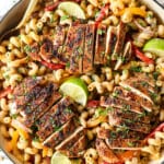 showing how to make jerk chicken pasta (Rasta pasta) by adding chicken to top of pasta with bell peppers