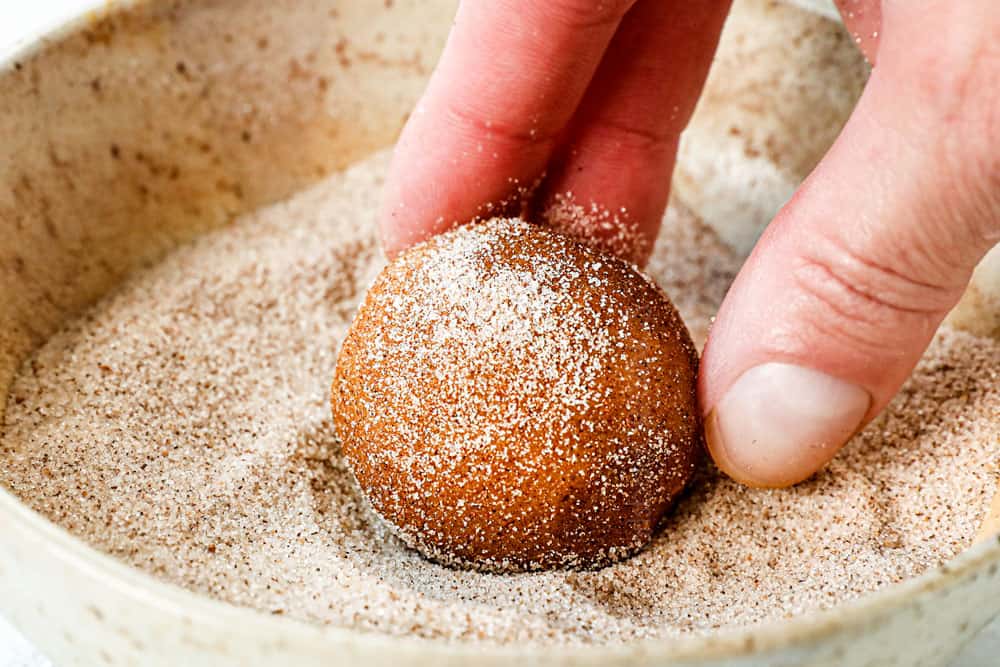 showing how to make pumpkin snickerdoodles by rolling pumpkin dough balls in cinnamon sugar