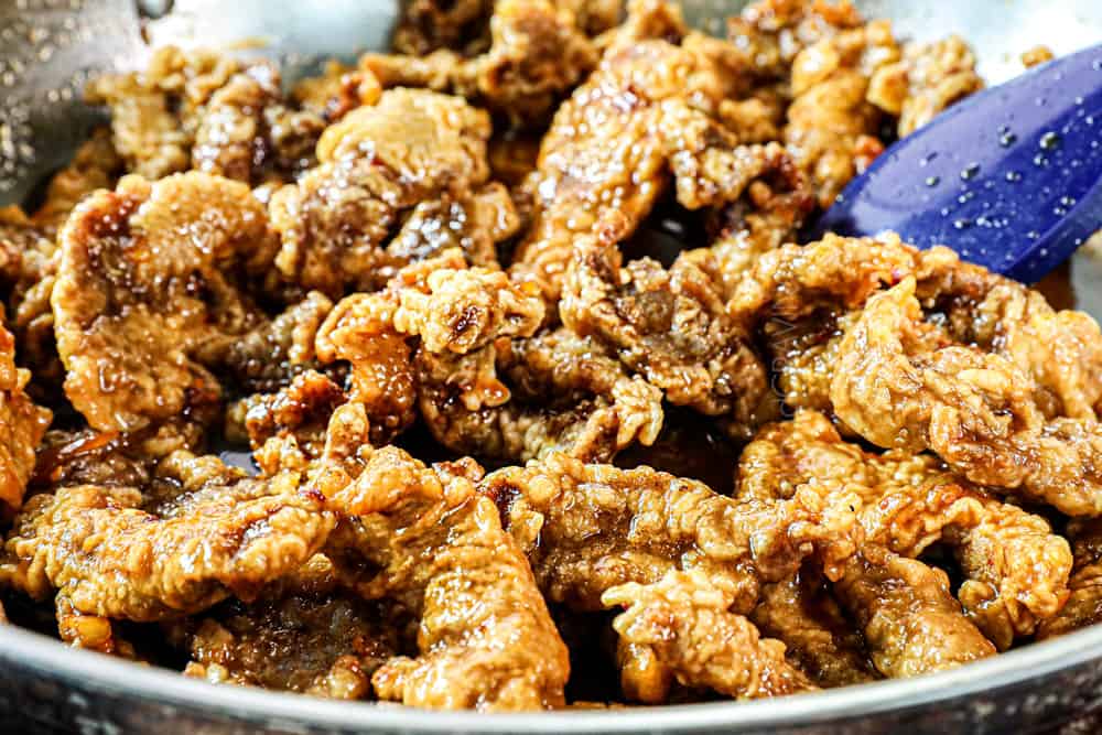 showing how to make crispy orange beef by stirring the crispy breaded beef with the orange sauce