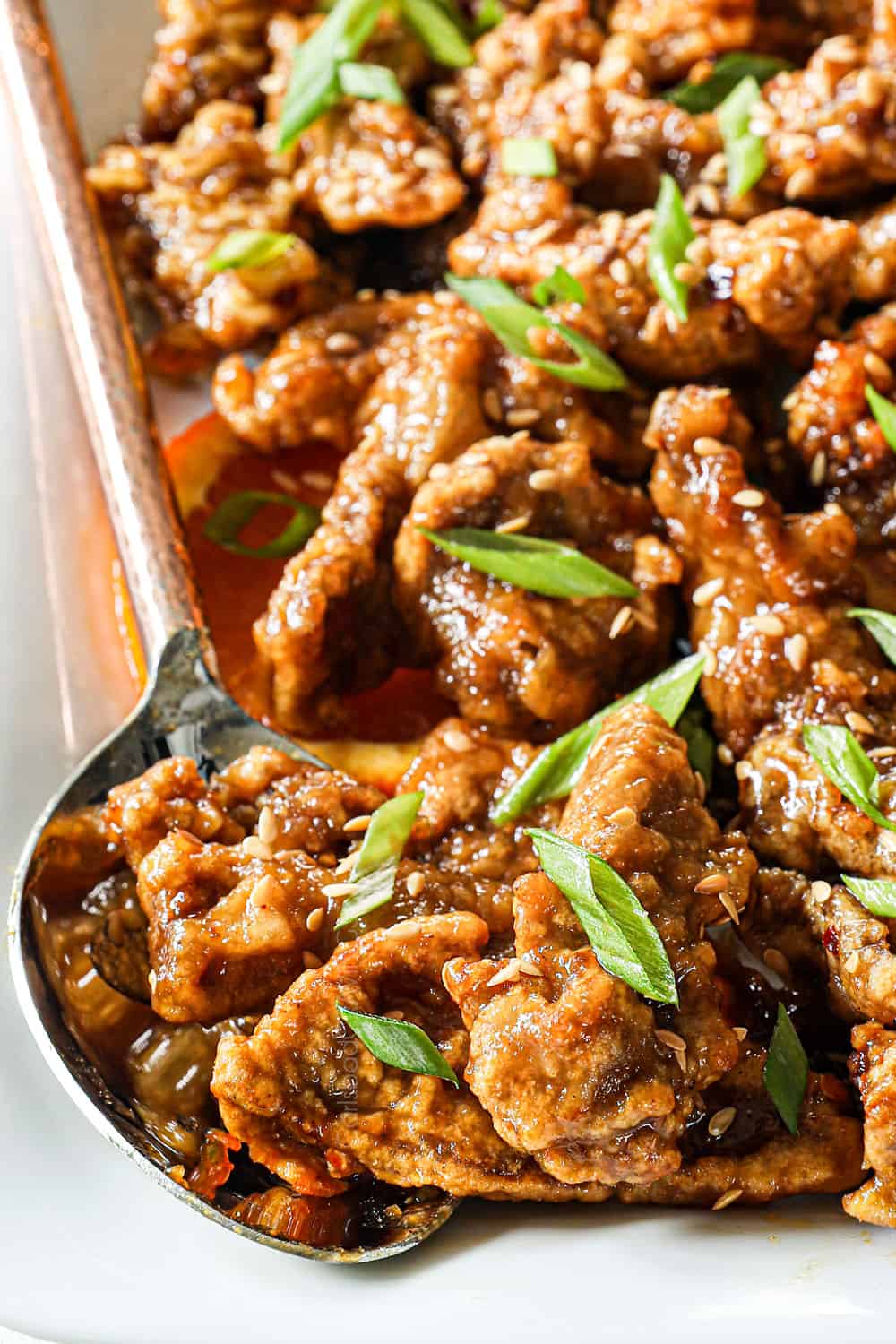 up close of a spoonful of orange beef on a platter garnished by green onions showing how crispy it is