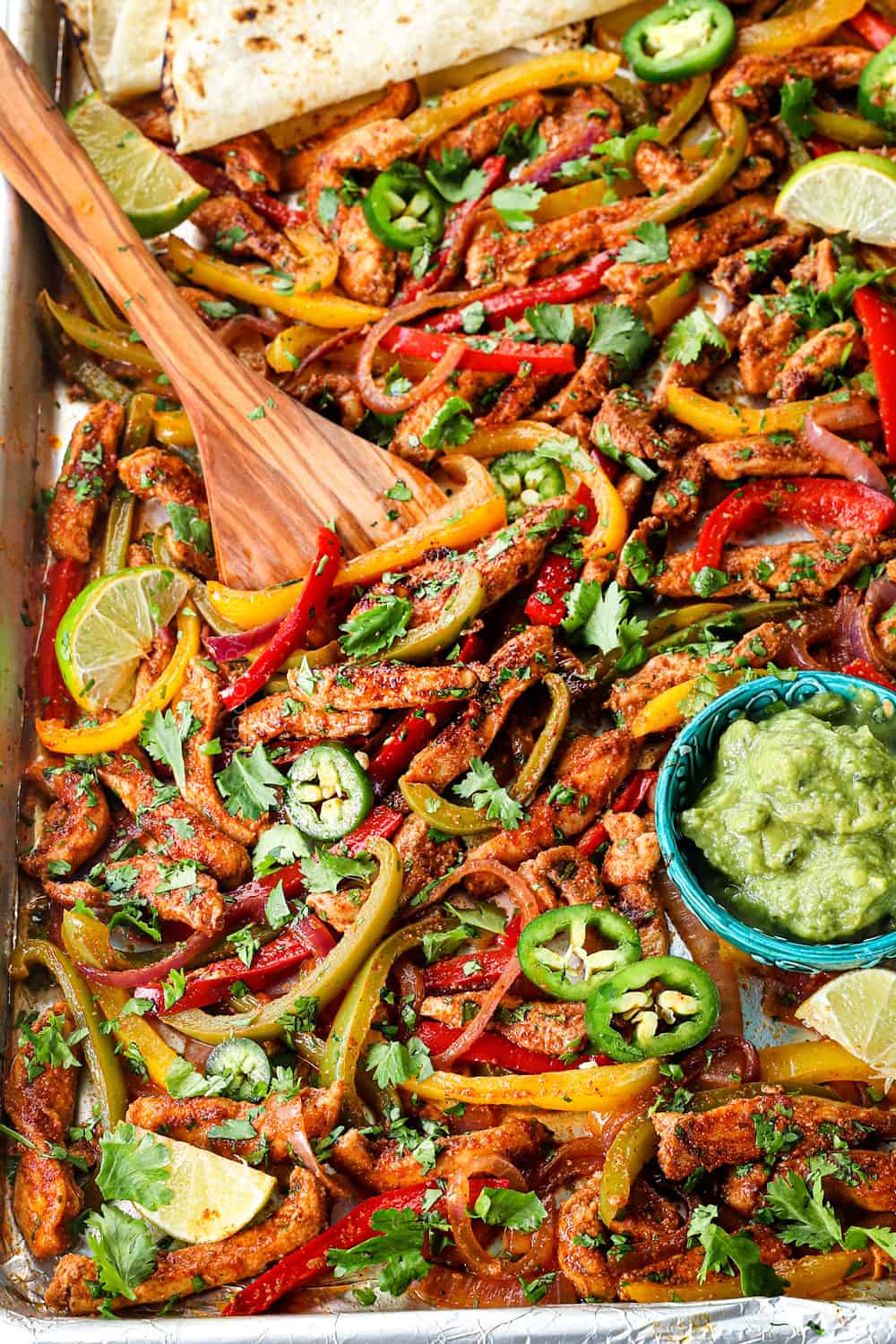 up close of scooping up sheet pan chicken fajitas to serve in flour tortillas