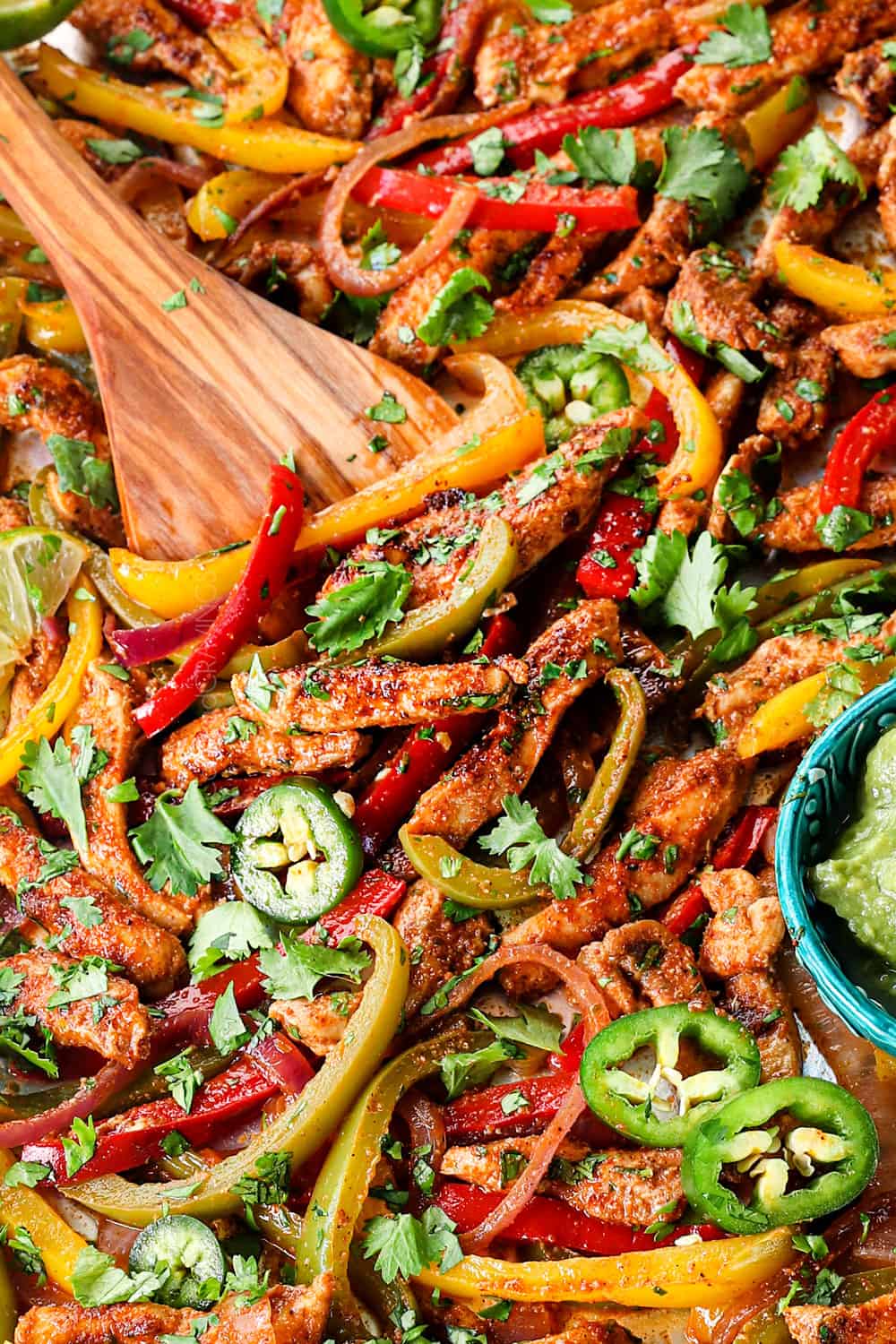up close of scooping up sheet pan chicken fajitas to serve in flour tortillas