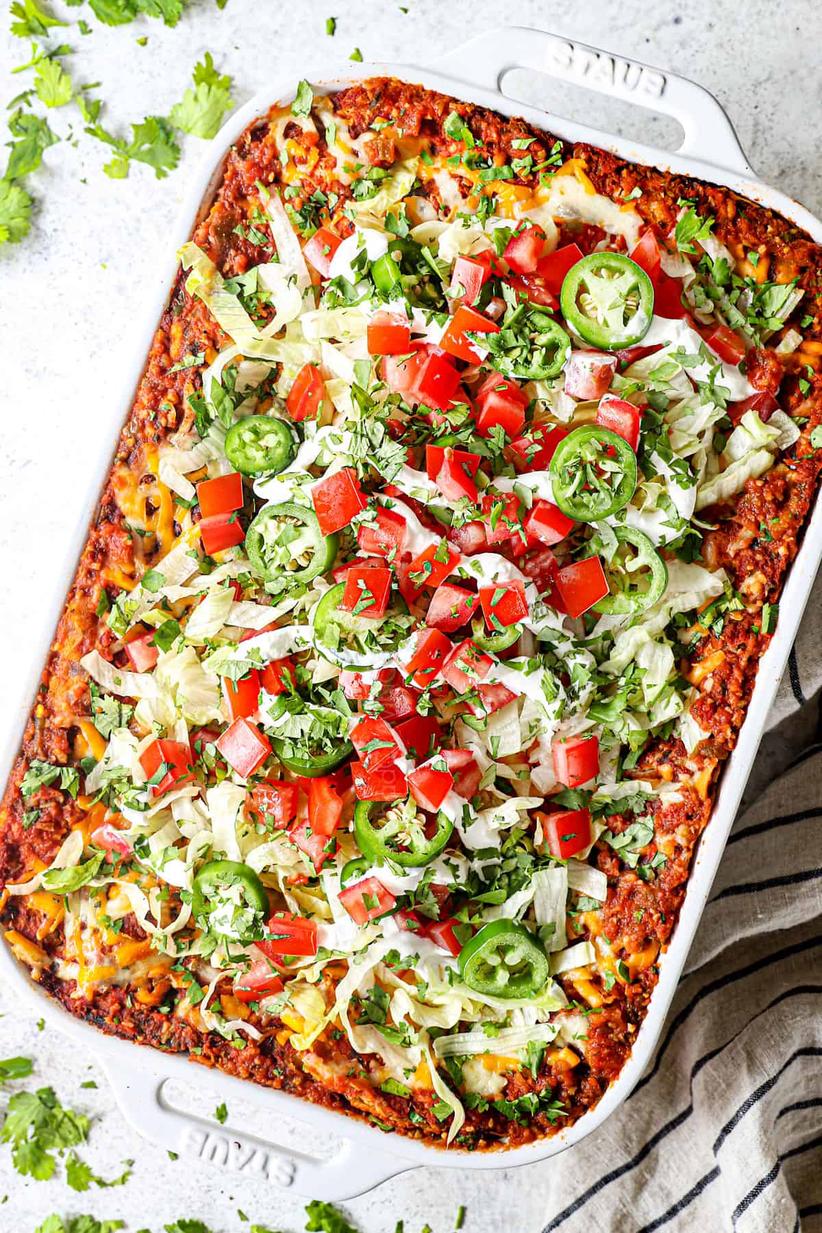 showing how to make taco lasagna by topping lettuce, tomatoes and cilantro
