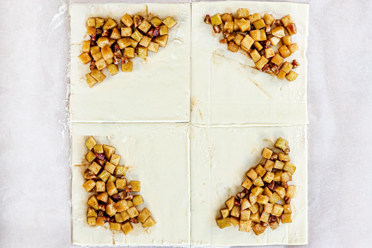 showing how to make apple turnovers recipe by adding apples to the corner of 4 squares of puff pastry