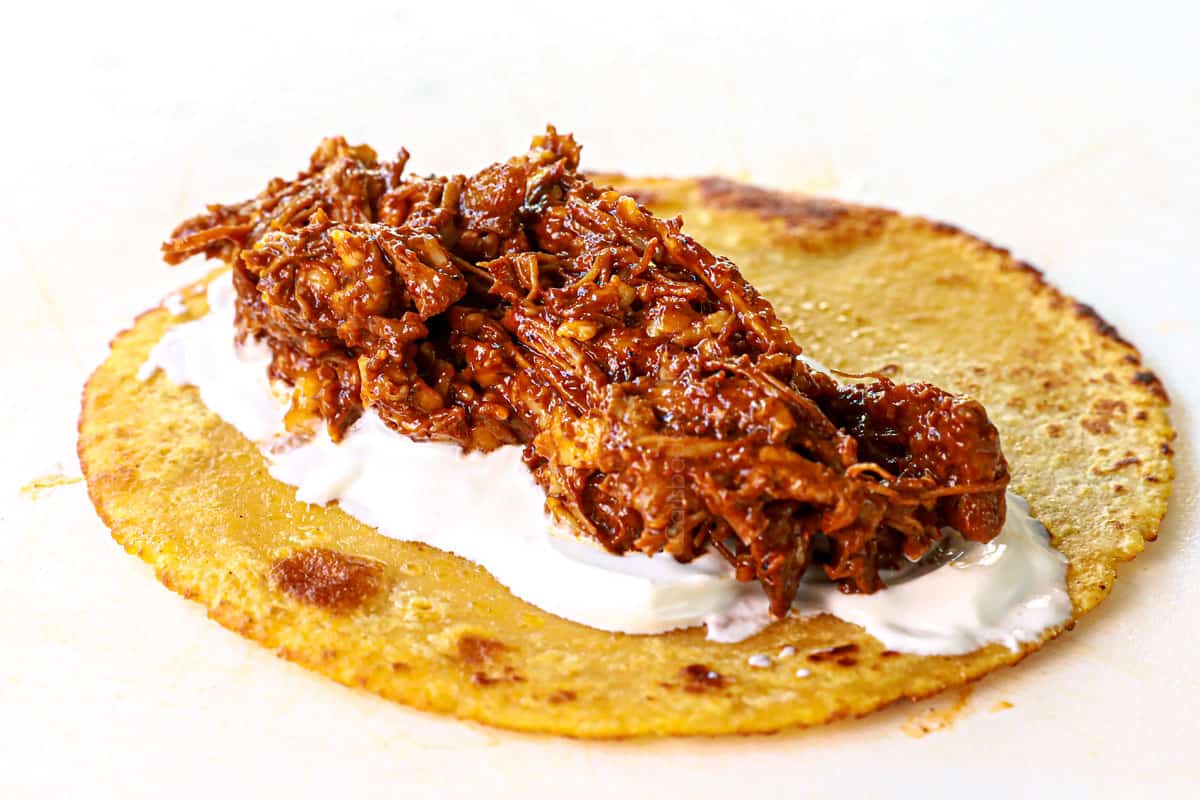 showing for the chicken mole enchiladas by adding sour cream and chicken mole to the tortilla