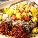 up close of serving chicken mole enchiladas on a plate with salsa and cotija cheese