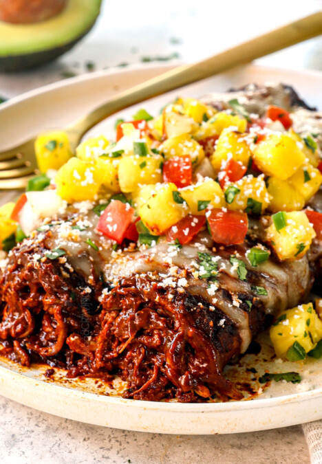 up close of serving chicken mole enchiladas on a plate with salsa and cotija cheese