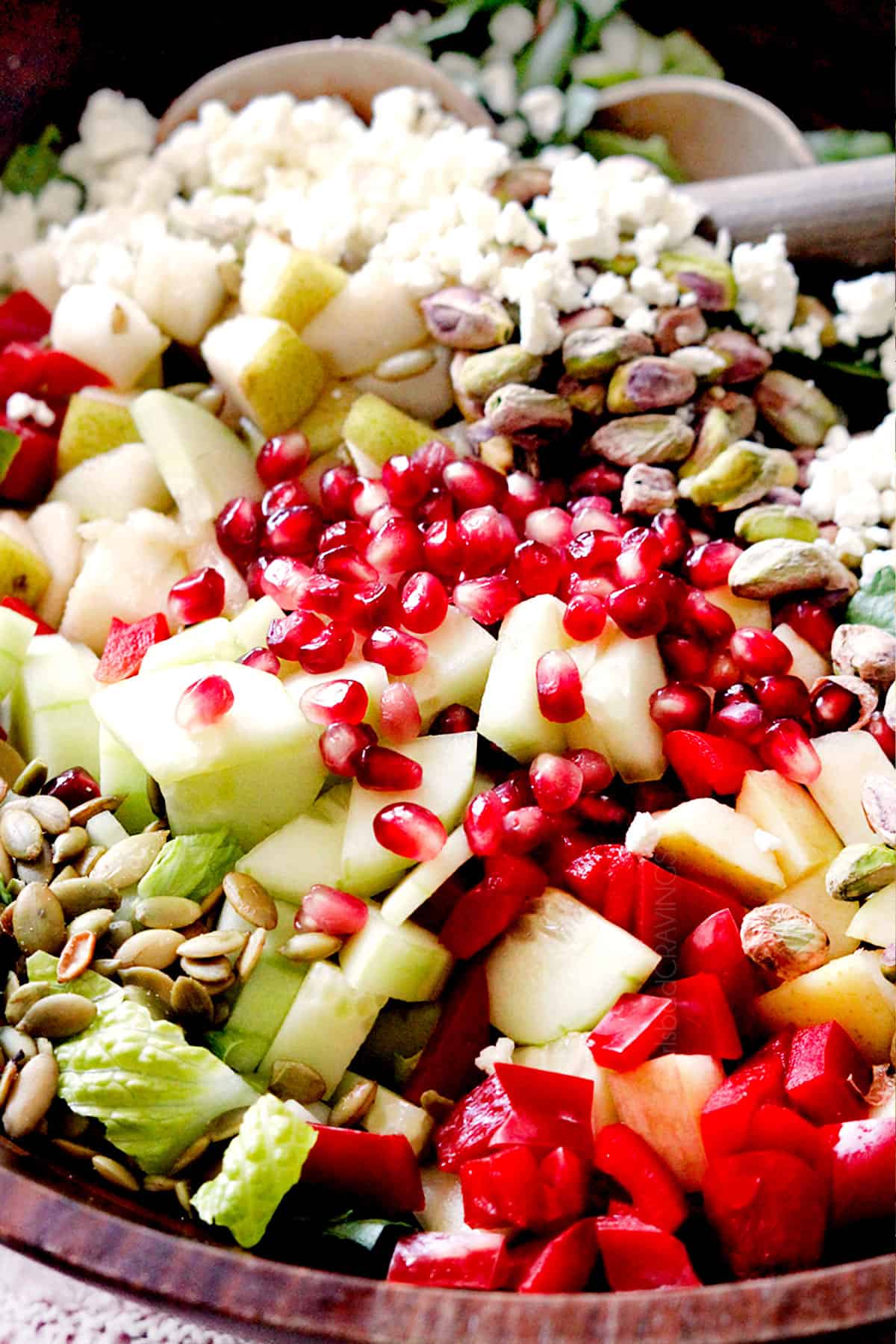 showing how to make pear salad with up close of ingredients in a bowl: pears, gorgonzola, pomegranate seeds, walnuts, cucumbers, red bell pepper and pepitas
