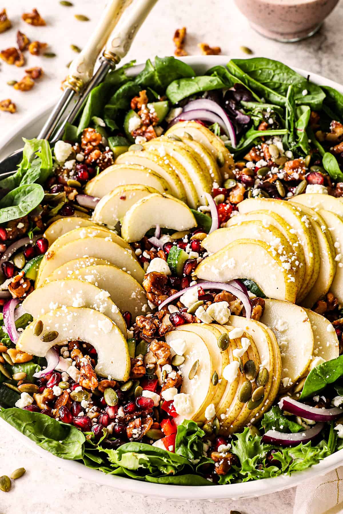 showing how to make pear salad by adding sliced pears, pomegranates, walnuts, gorgonzola, red onions and spinach to a bowl
