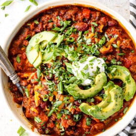 top view of pumpkin chili in a bowl with sour cream cheese, avocados and cilantro