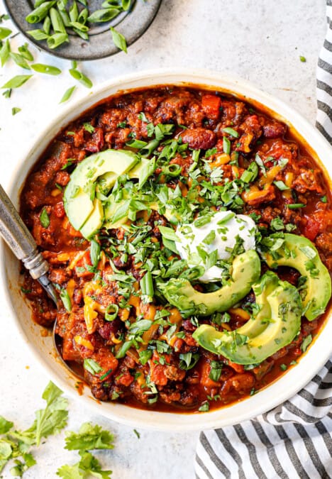 top view of pumpkin chili in a bowl with sour cream cheese, avocados and cilantro