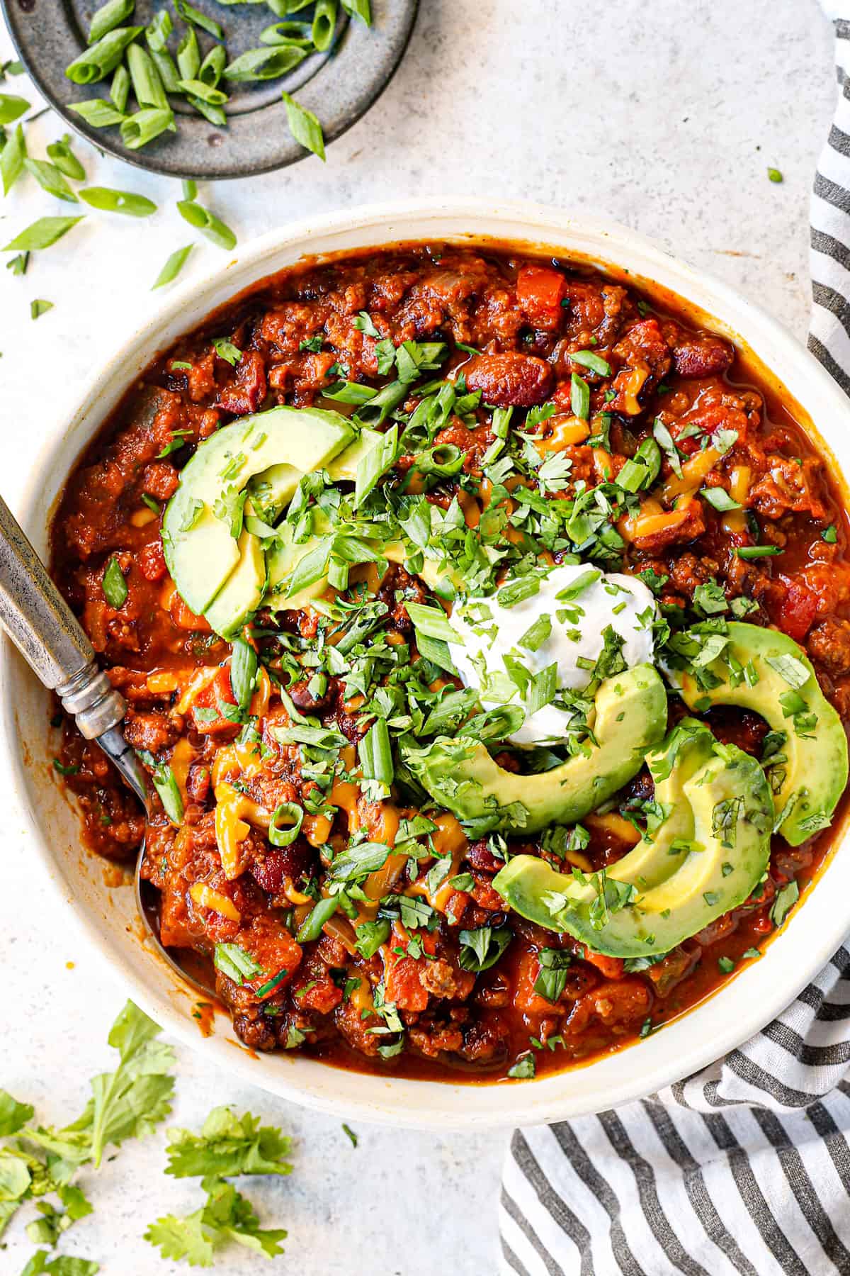 top view of pumpkin chili in a bowl with sour cream cheese, avocados and cilantro