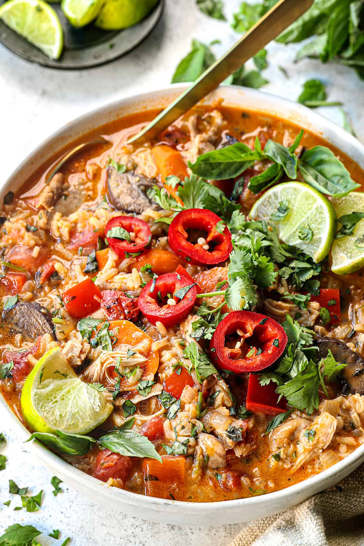 showing how to serve Thai coconut curry soup with chicken by adding to a bowl and garnishing with limes, cilantro and chili peppers