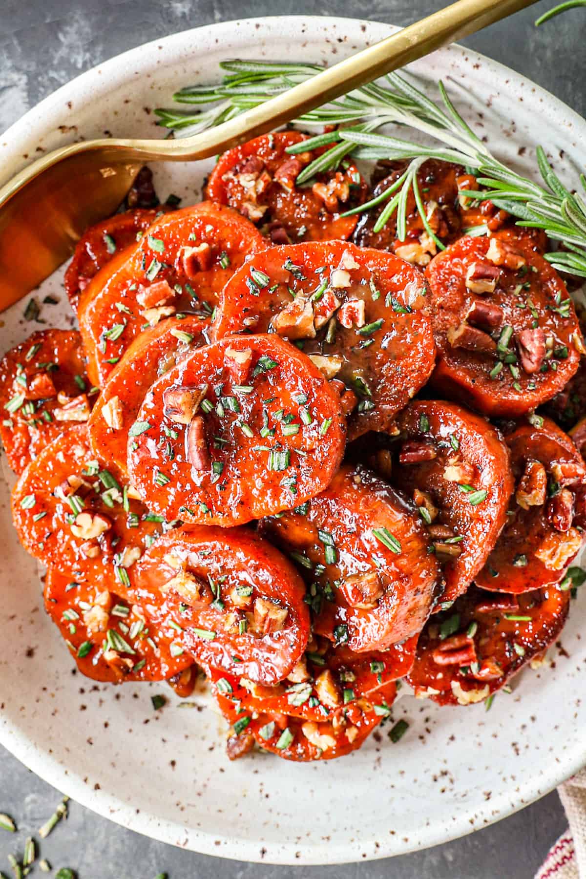 top view of candied yams recipe (candied sweet potato recipe) in a bowl garnished with pecans and herbs
