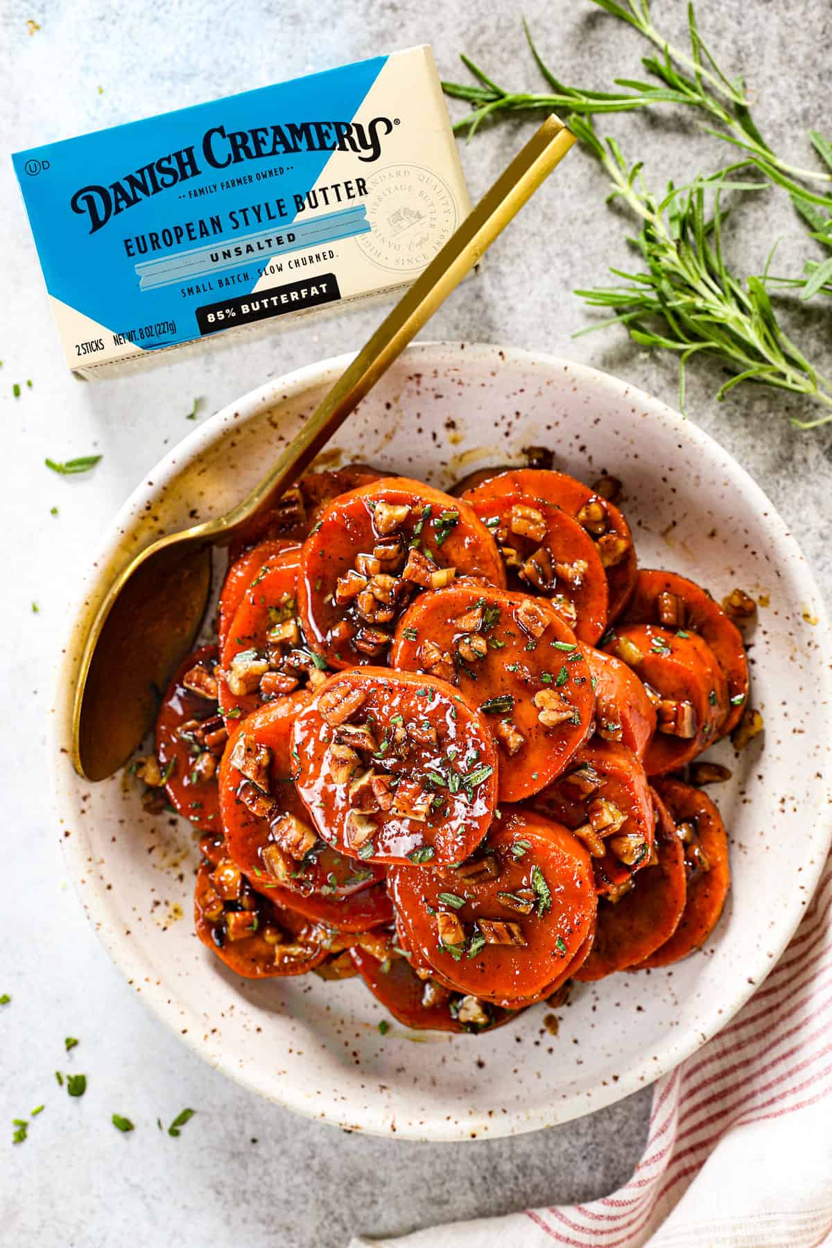 top view of candied yams recipe (candied sweet potato recipe) in a bowl with syrup over top garnished with pecans and herbs