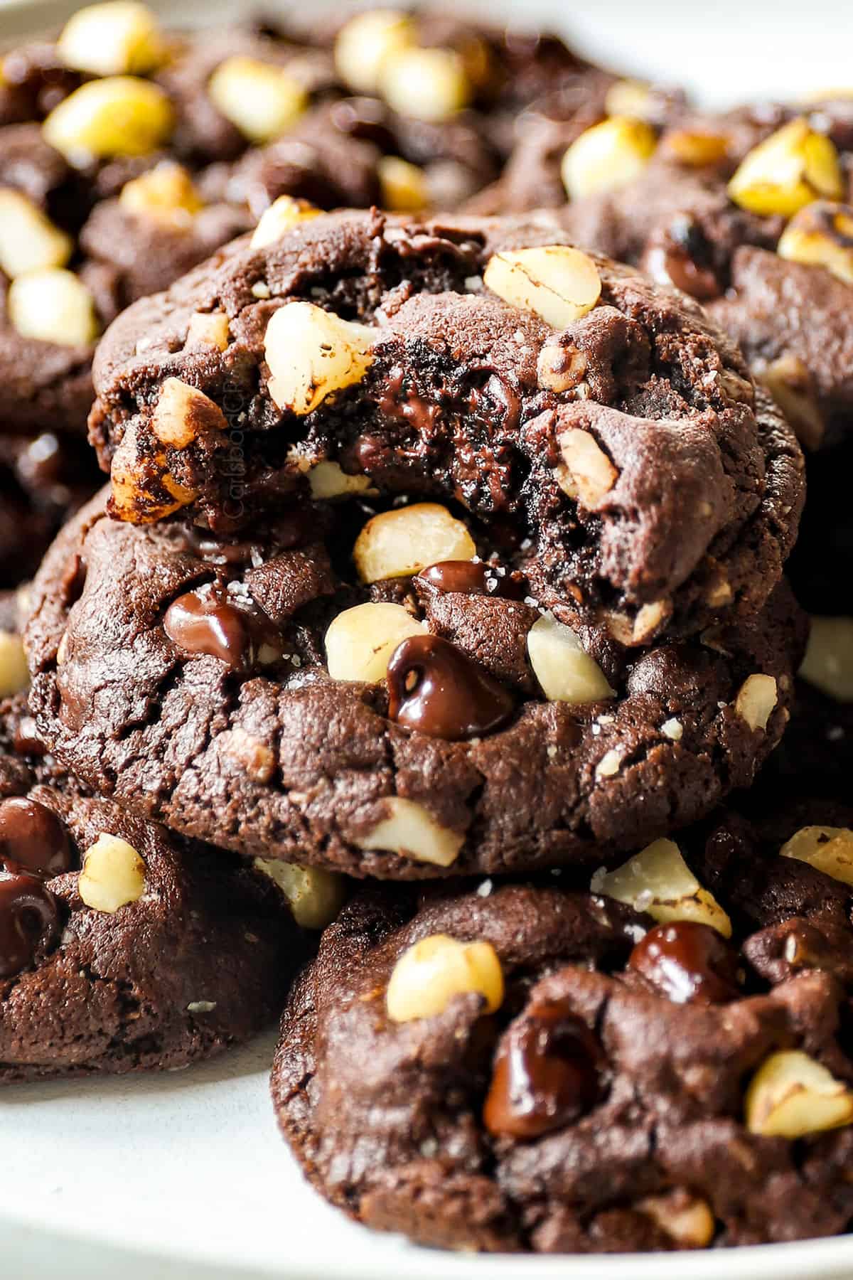 a plate of macadamia nut cookies with a cookie with a bite take out showing the melted chocolate inside