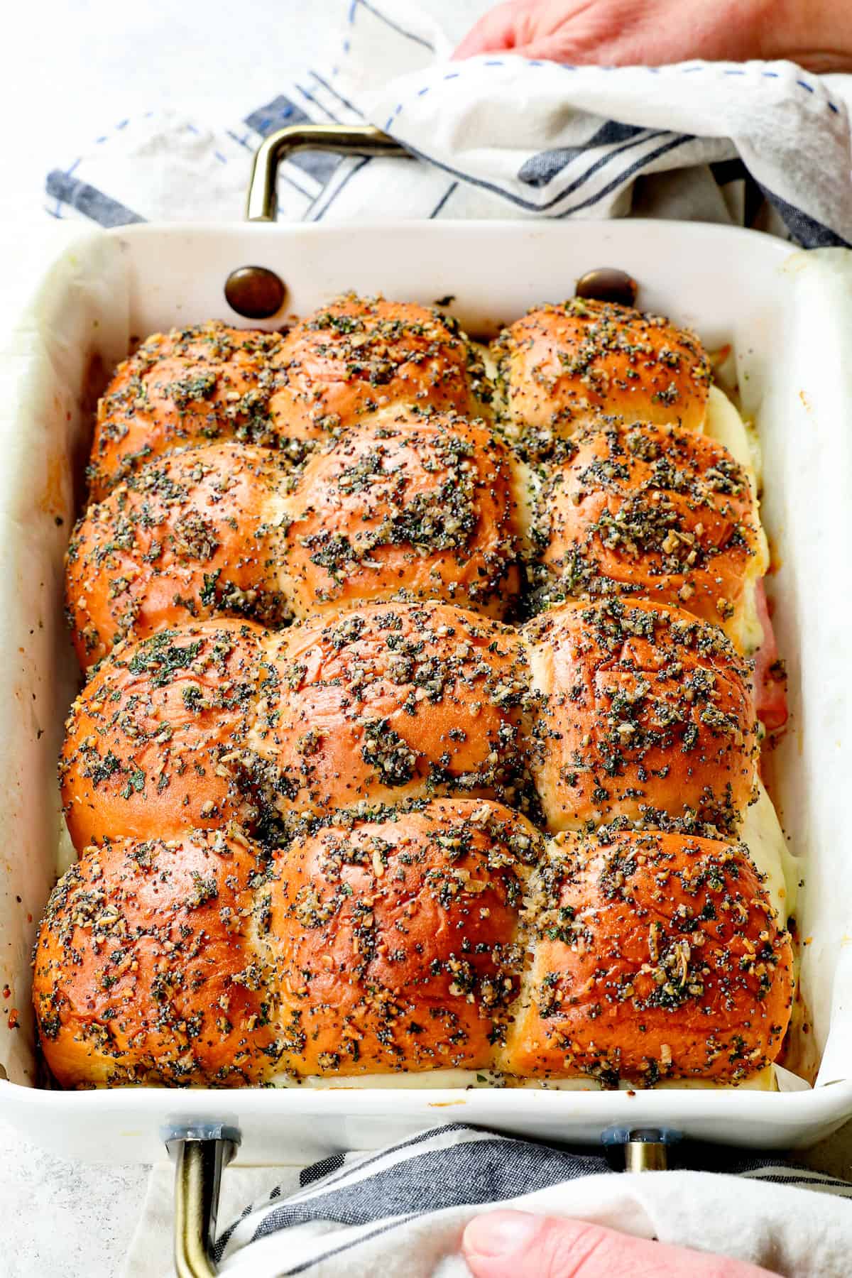 two hands holding a pan of baked ham and cheese sliders recipe on Hawaiian rolls