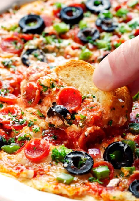 up close of scooping up baked pizza dip with a baguette slice