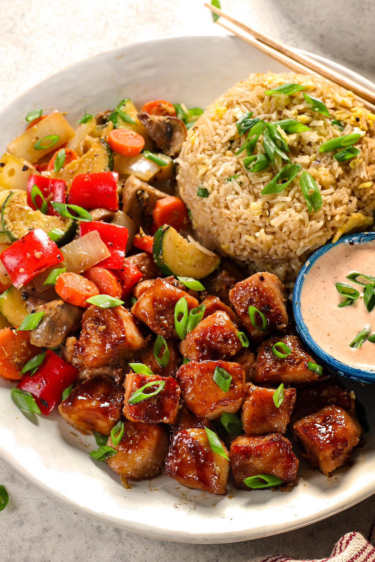 showing how to make chicken hibachi by adding to a plate with stir fried vegetables, fried rice and yum yum sauce