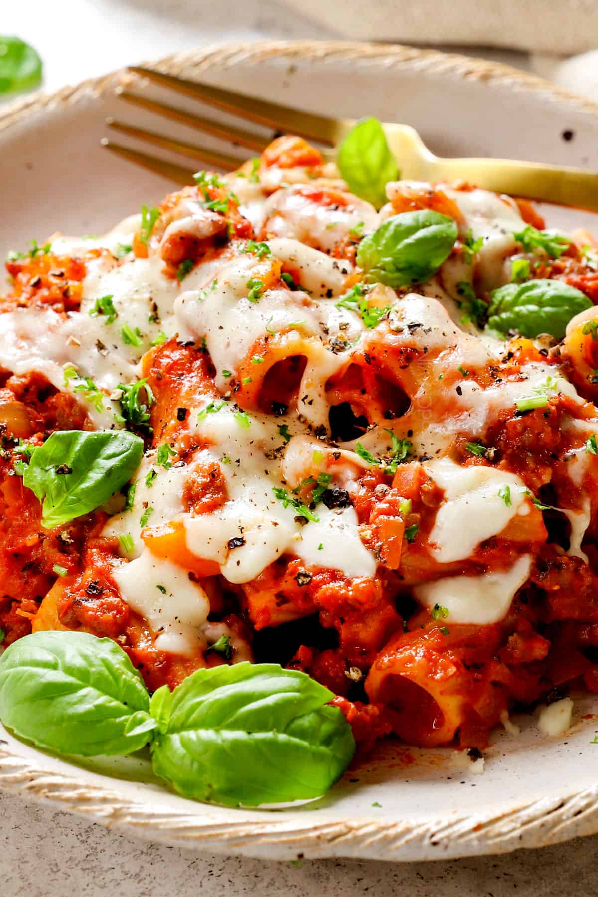 showing how to serve baked rigatoni by adding to a plate and garnishing with Parmesan and basil