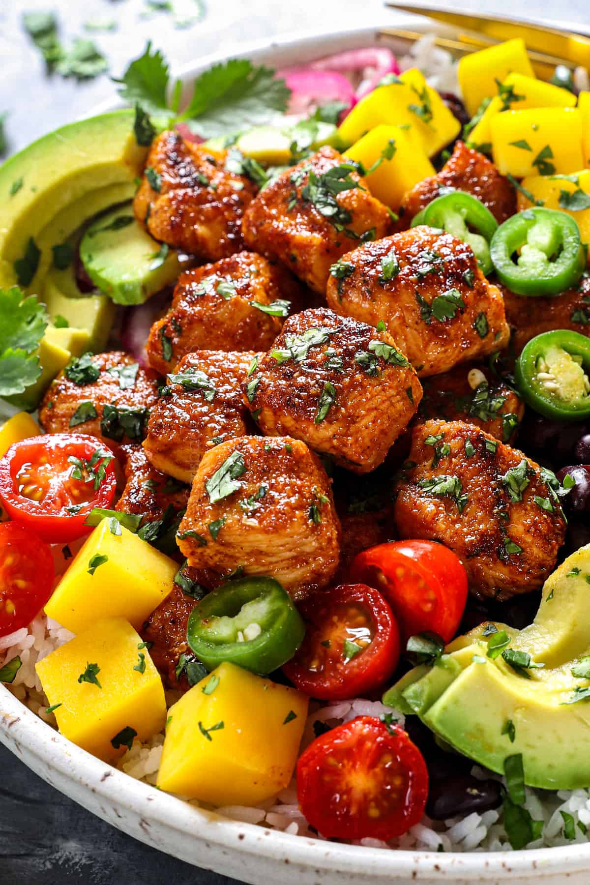 up close of chicken bites recipes in a bowl with rice, tomatoes and avocado