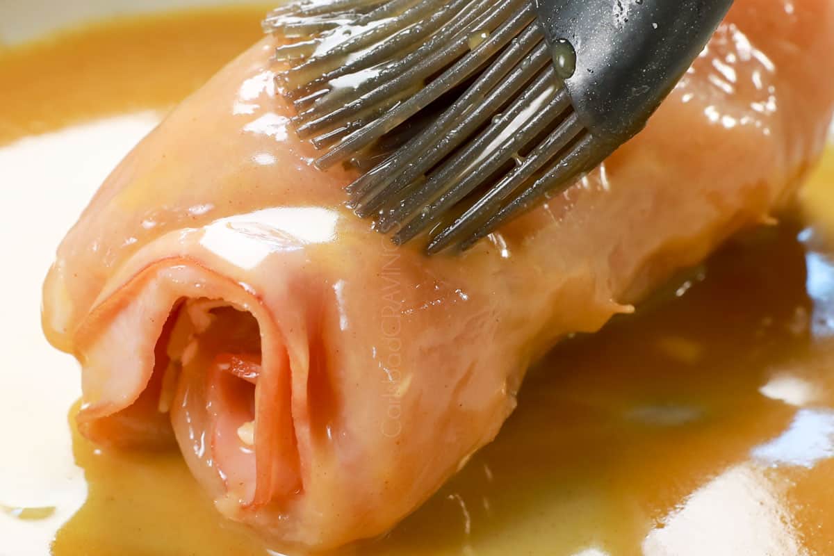 showing how to make chicken cordon bleu recipe by brushing chicken with Dijon coating before adding the panko