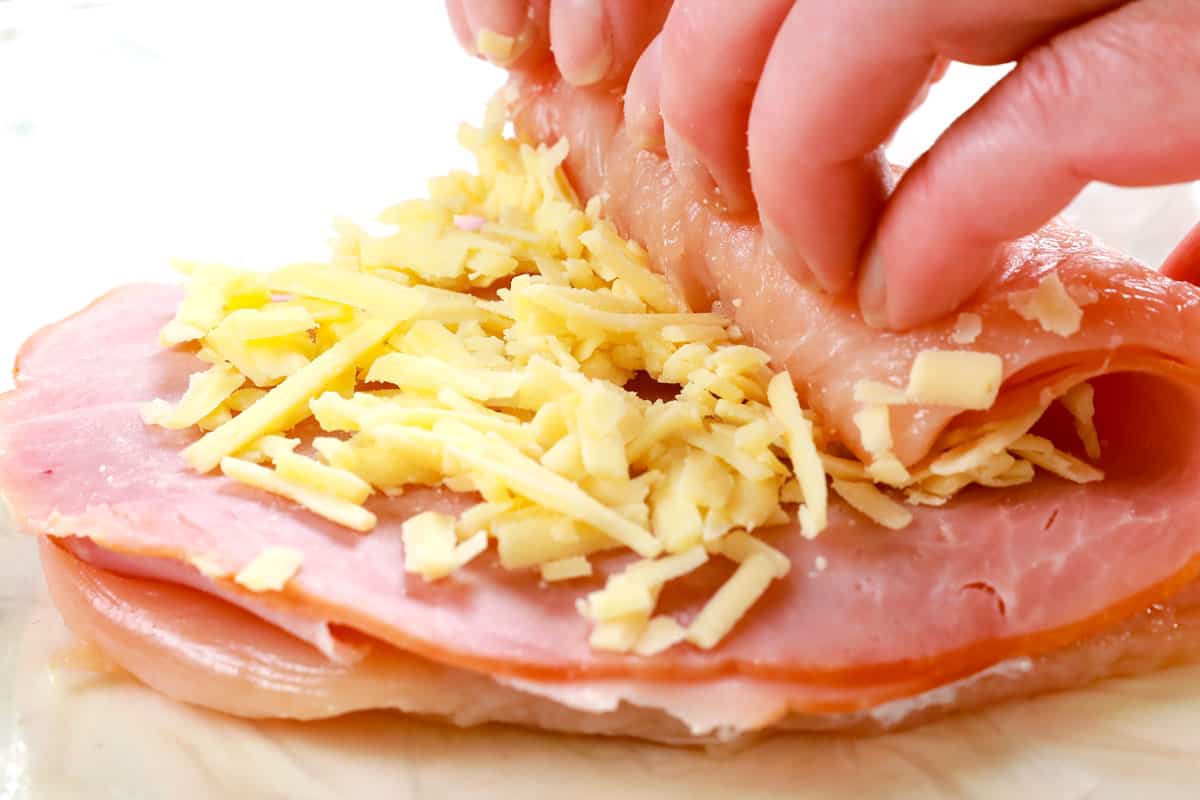 showing how to make chicken cordon bleu recipe by rolling the chicken, ham and cheese up tightly