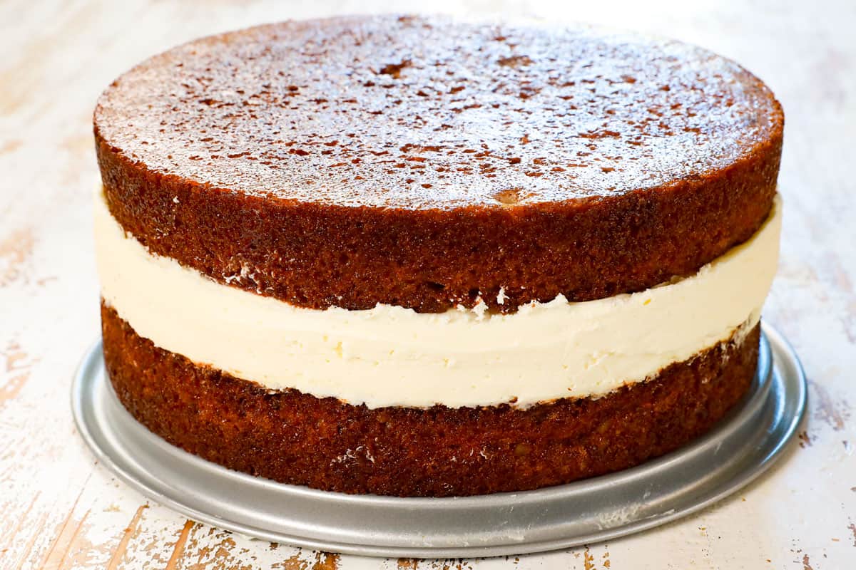 showing how to make carrot cake cheesecake by layering the cheesecake on top of baked carrot cake