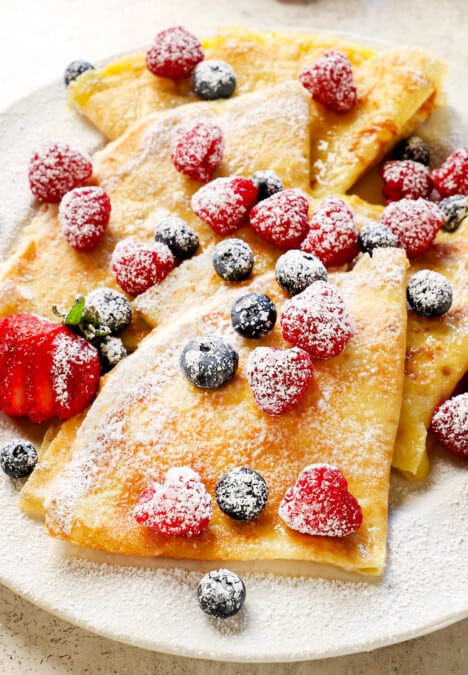 serving crepes with berries, cream and powdered sugar