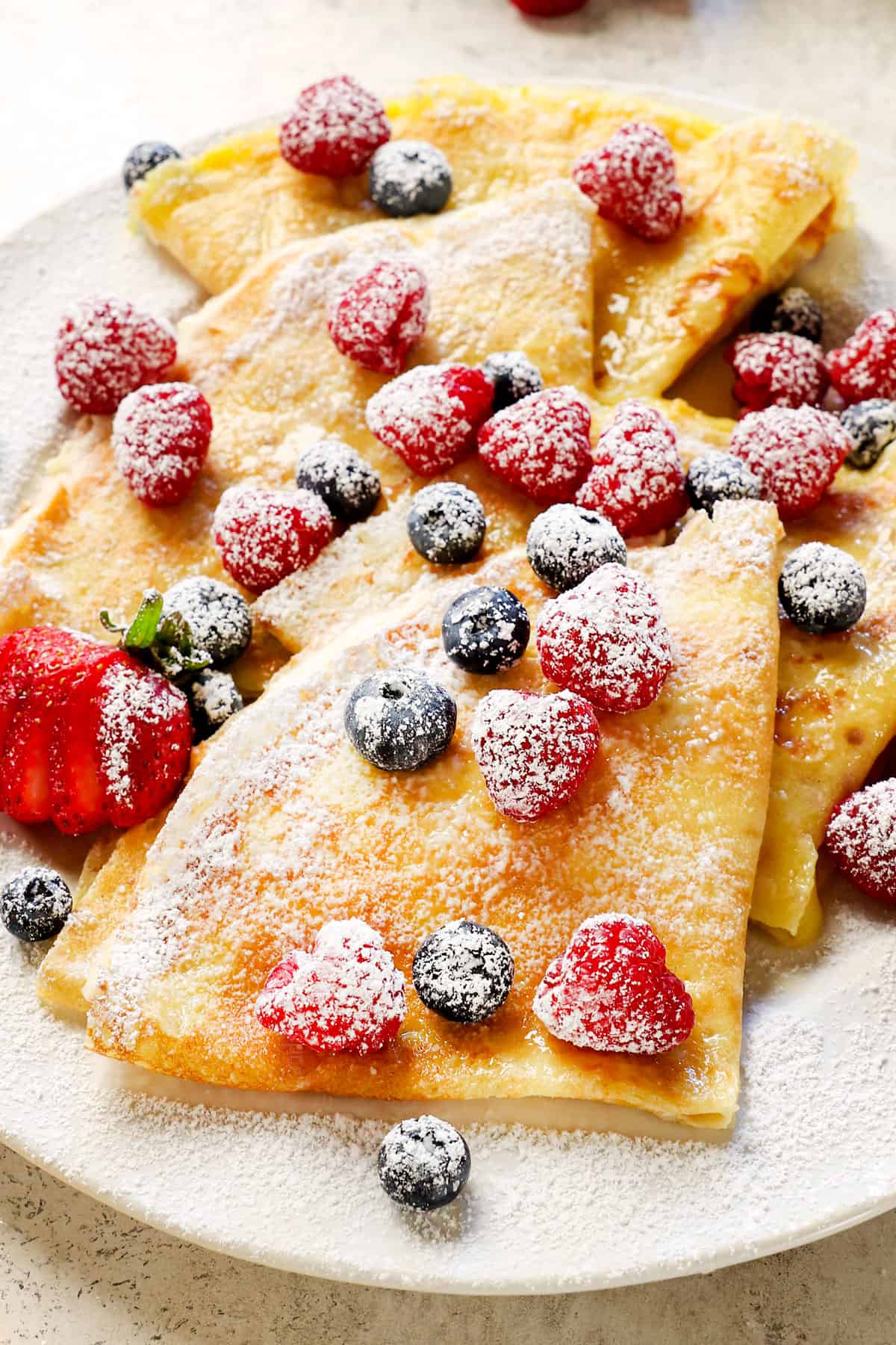 serving crepes with berries, cream and powdered sugar