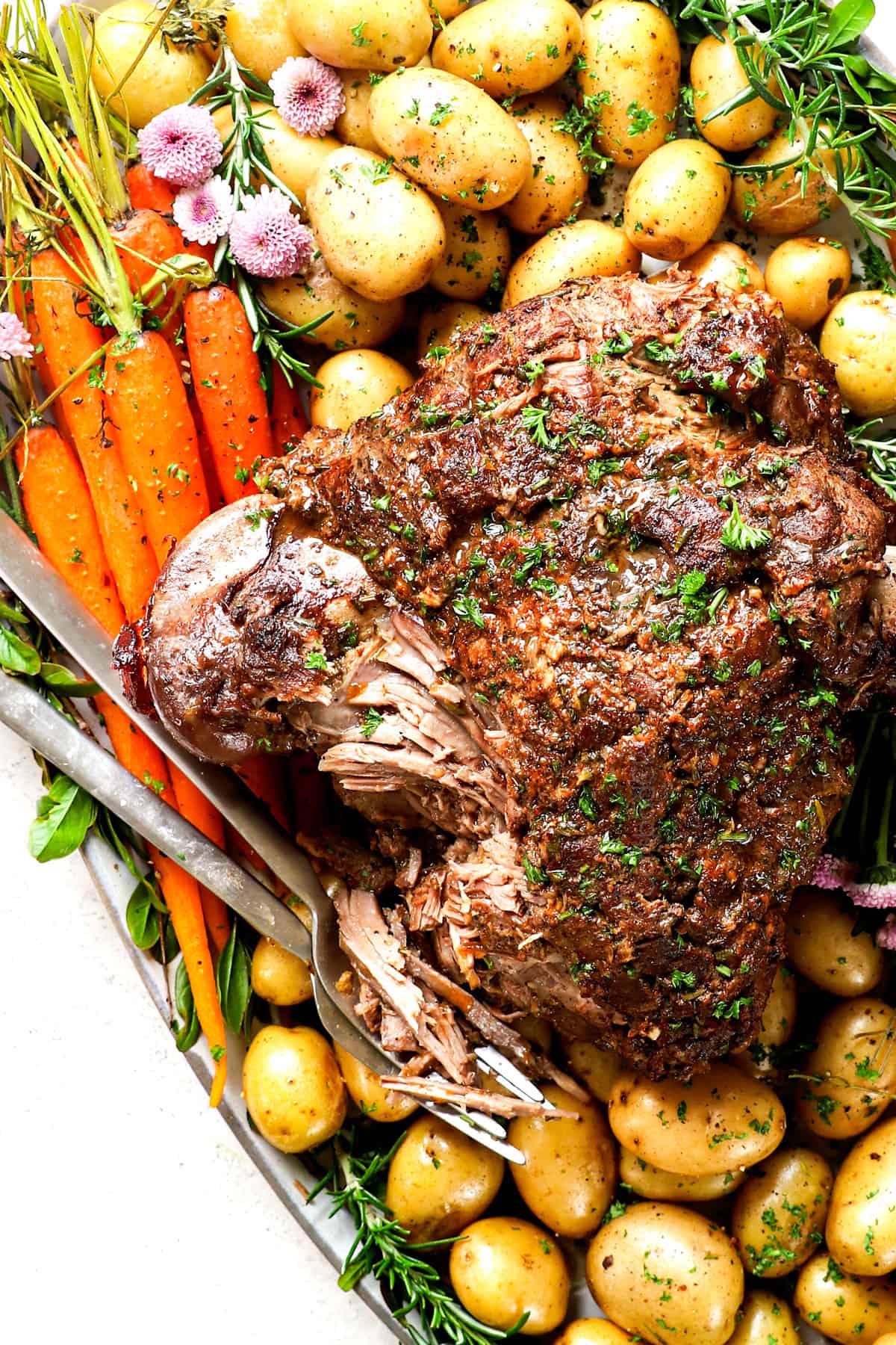 showing how to serve roast leg of lamb on a platter with carrots and potatoes
