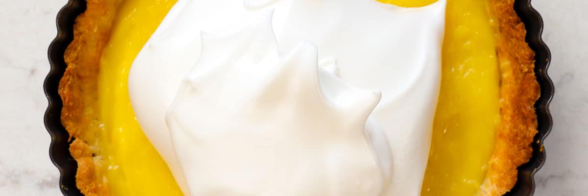 showing how to make easy lemon meringue pie recipe by adding the lemon meringue to the lemon filling in the pie shell