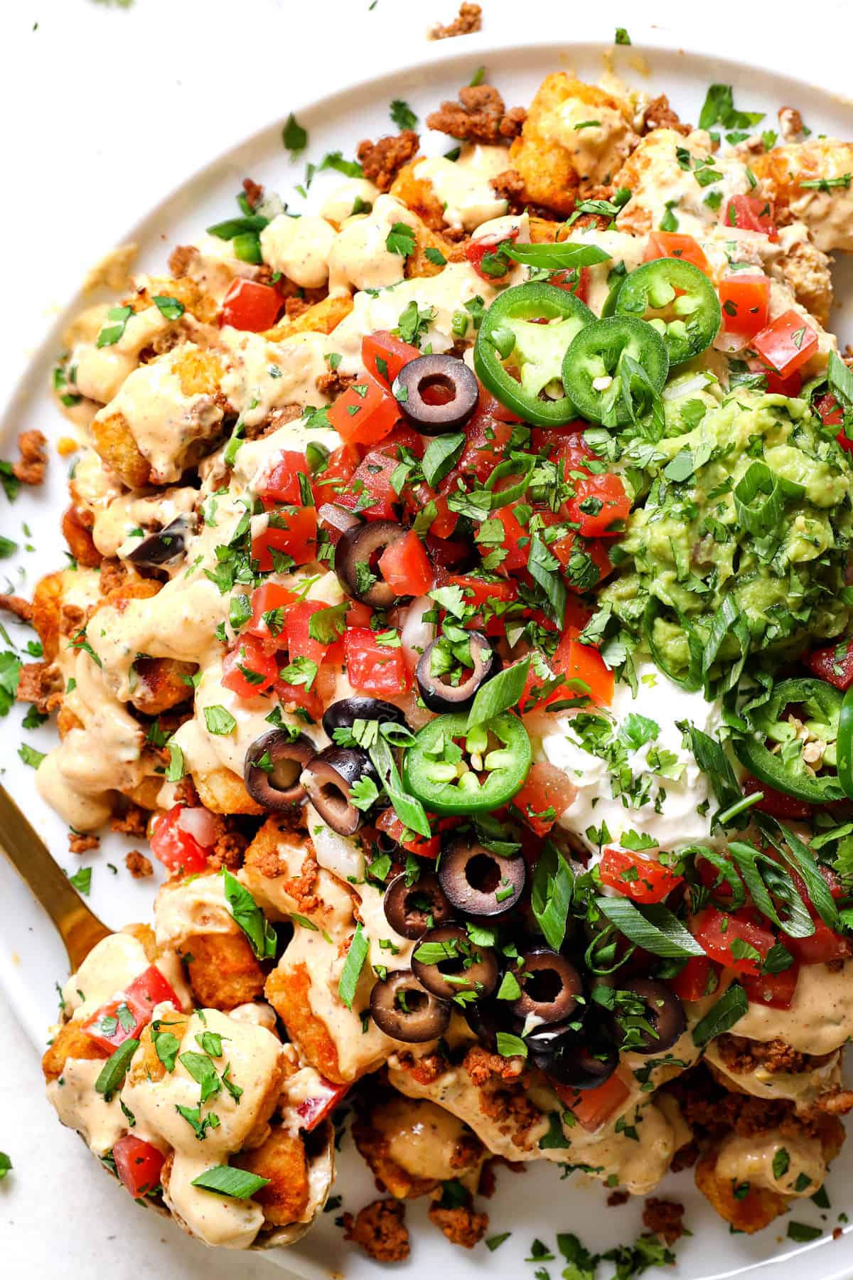 showing how to make tater tot nachos (totchos) by topping with pico de gallo, guacamole, sour cream, olives, cilantro and jalapenos