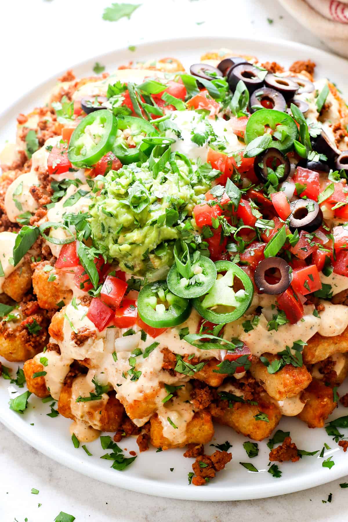 showing how to serve totchos (tater tot nachos) by adding to a platter and garnishing with cilantro, jalapenos and pico de gallo