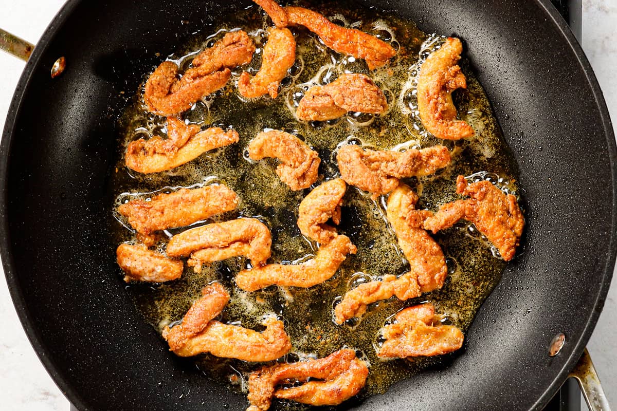 showing how to make spicy Dragon Chicken by pan frying the chicken strips until crispy