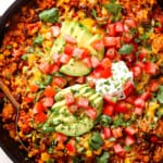 showing how to make chicken fiesta recipe by topping the skillet with sour cream, avocados and pico de gallo