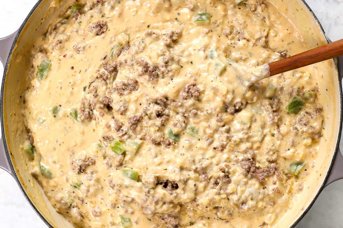 showing how to make Philly Cheesesteak Pasta by stirring ground beef in to the cheesy sauce.