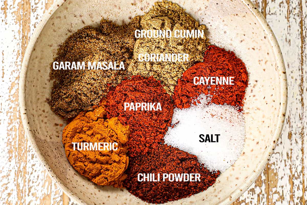 showing how to make butter chicken recipe easy by mixing together garam masala, ground cumin, coriander, paprika, cayenne, salt, chili powder and turmeric
