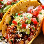 up close of chicken street tacos showing what they're made of: corn tortilla, chopped chicken, guacamole, pico de gallo and cotija cheese