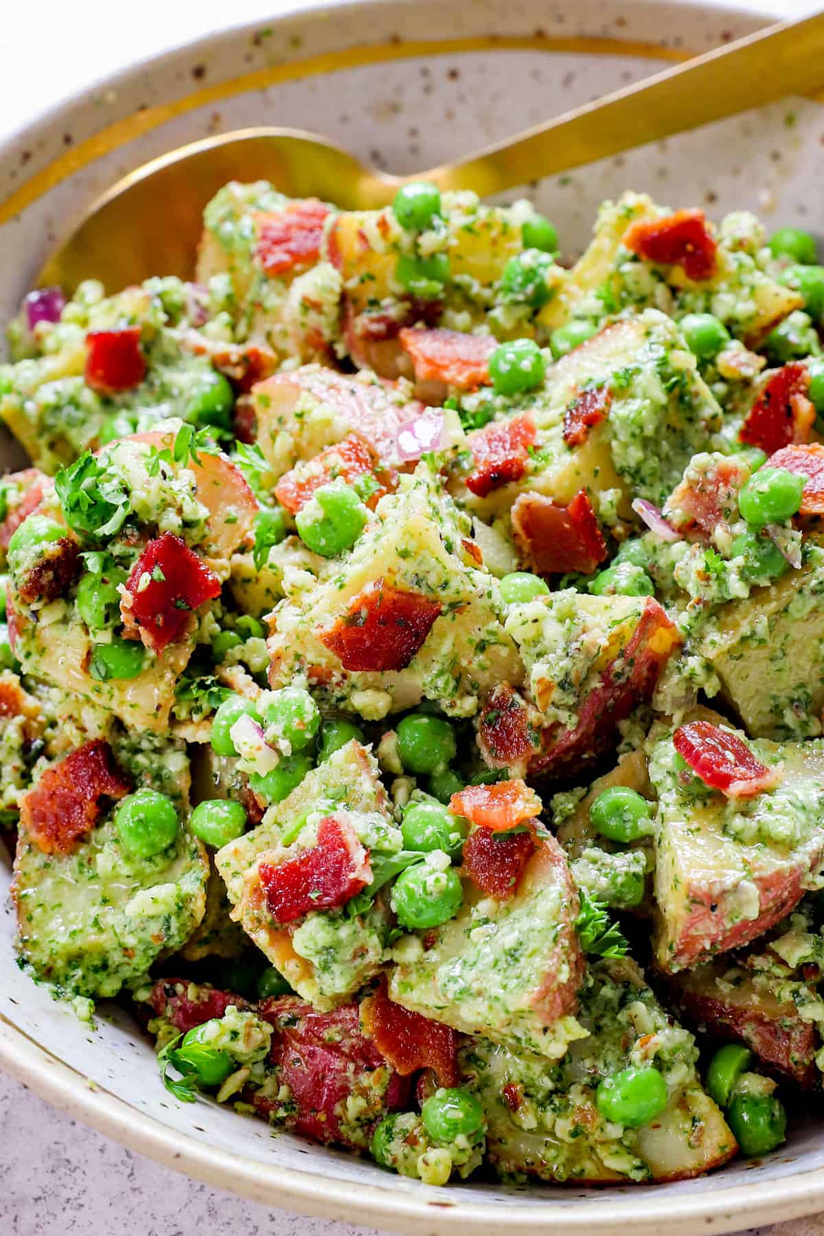 up close of red skinned potato salad in serving bowl with bacon and peas