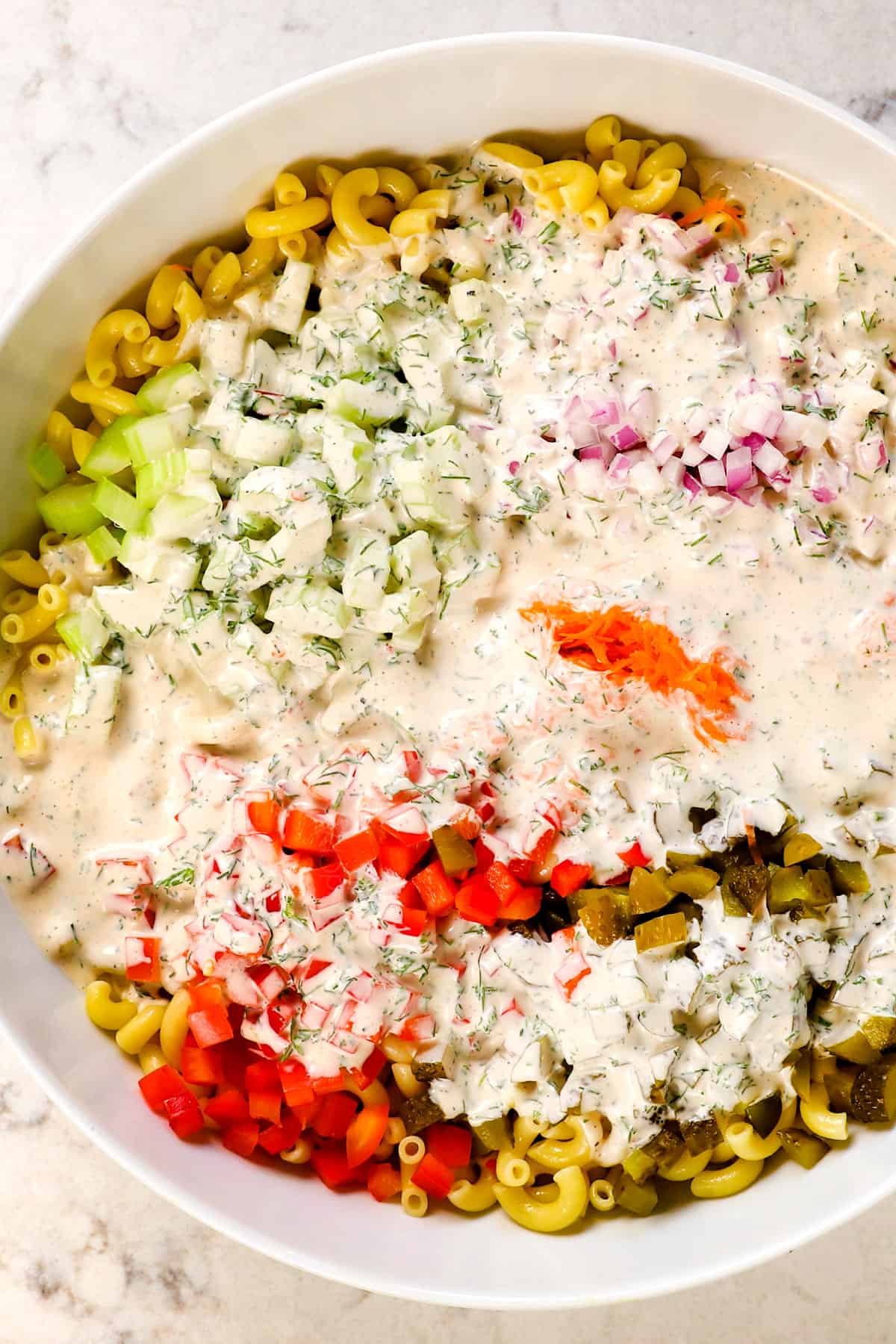 showing how to make macaroni salad by pouring the dressing over the salad ingredients in a bowl