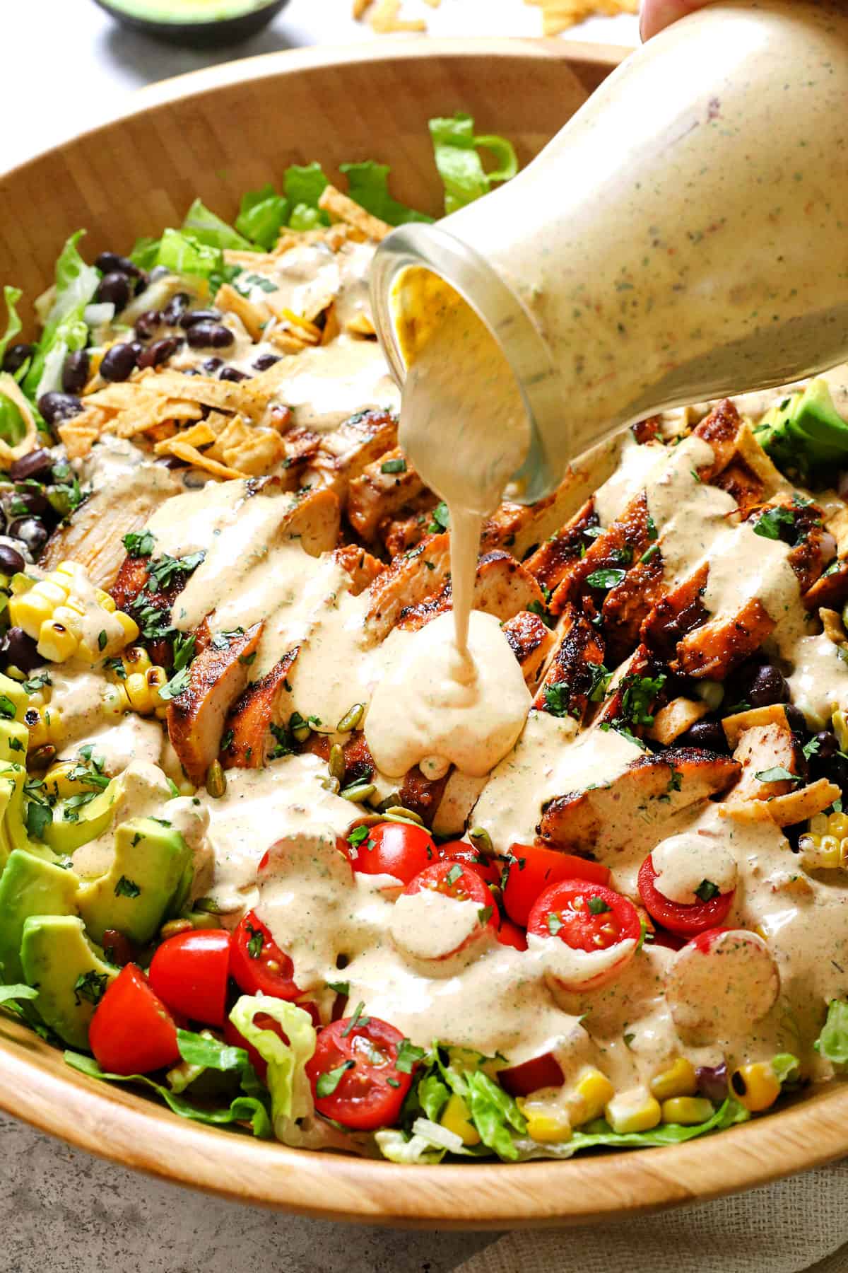 showing how to make Southwest Chicken Salad by drizzling dressing over the salad