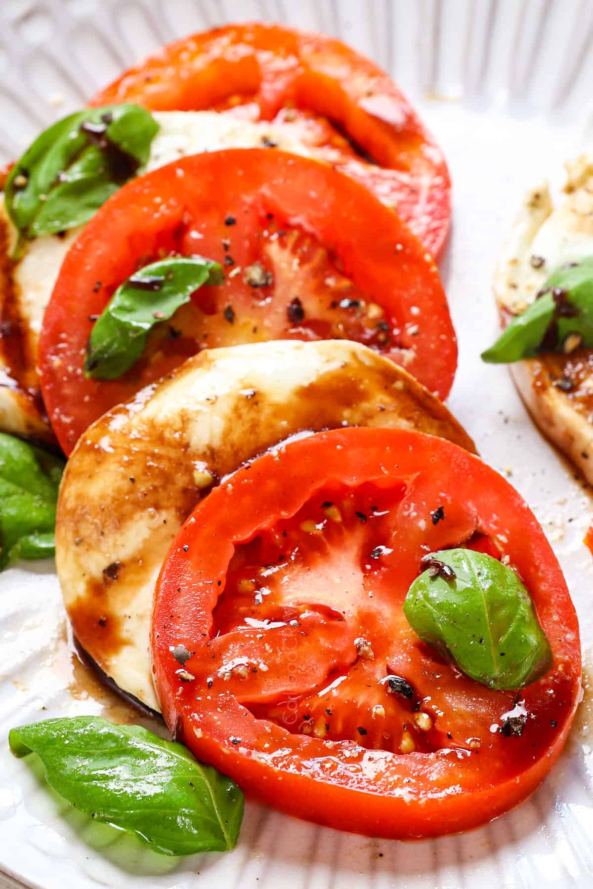 showing how to serve Caprese Salad recipe by adding tomatoes and mozzarella to a plate with basil