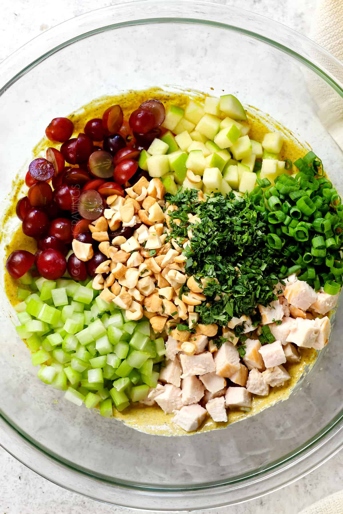showing how to make curry chicken salad by adding chicken, celery, grapes, apples, nuts, green onions and cilantro to the dressing