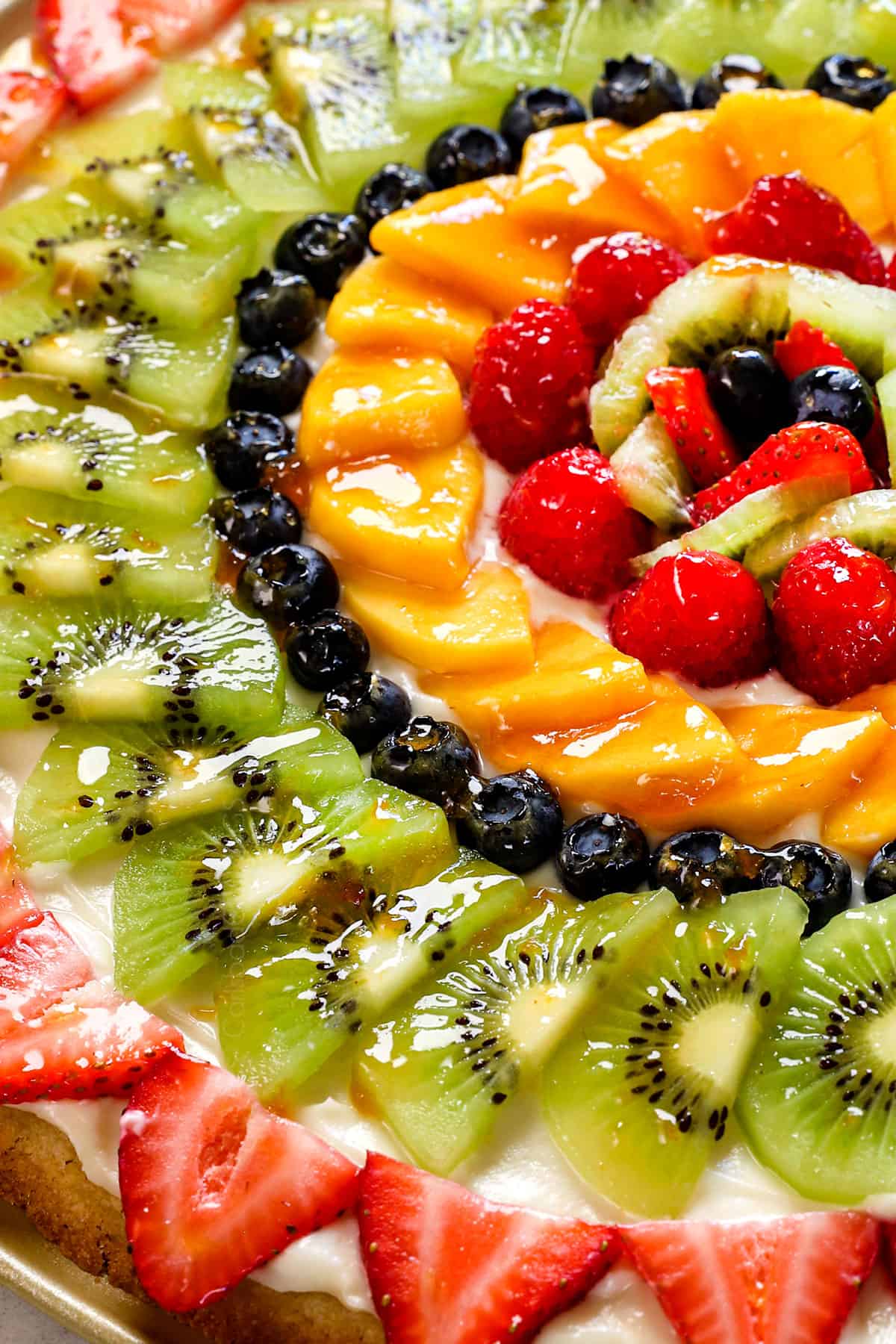 up close of sugar cookie fruit pizza with strawberries, kiwis, blueberries, mangos and raspberries