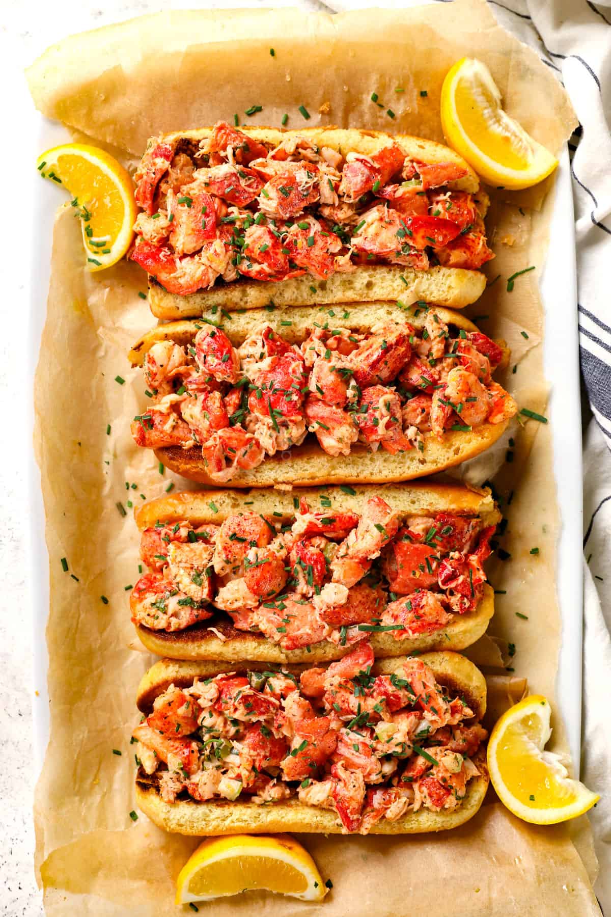 showing how to make a lobster roll by dividing the lobster meat between the rolls