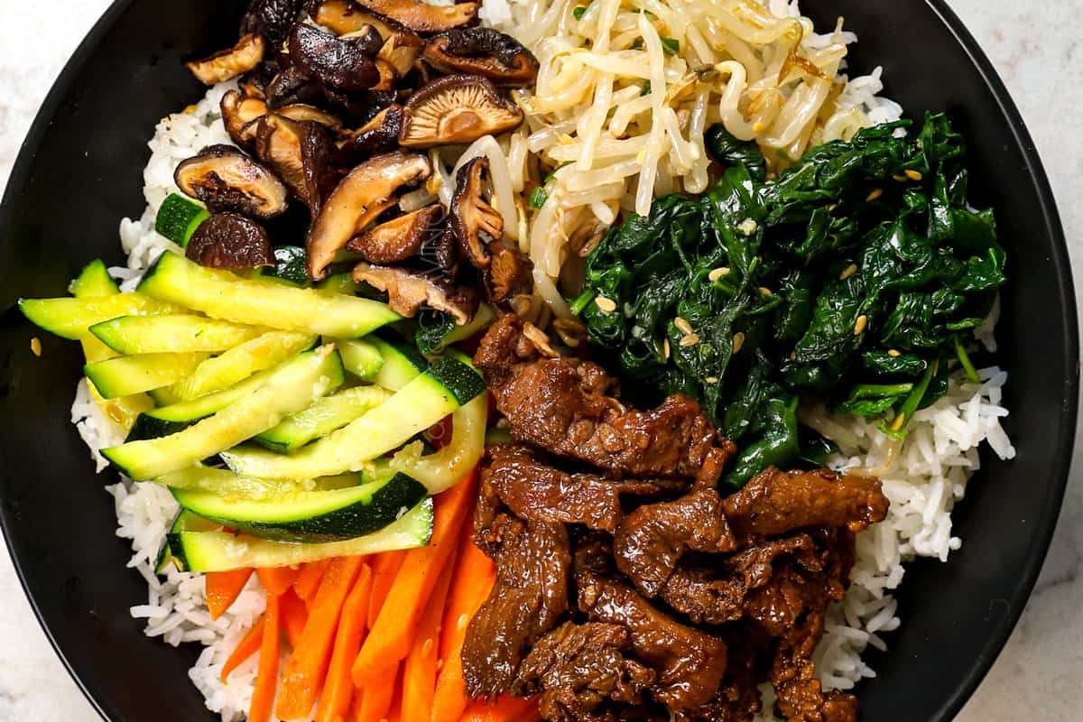 showing how to make bibimbap bowls by adding rice to a bowl and topping with vegetables